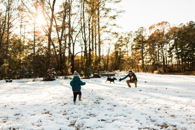 Girl walking on snow covered landscape with father against trees