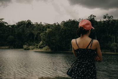 Rear view of woman standing by lake against sky