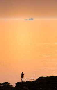 Silhouette woman standing on shore against sky during sunset