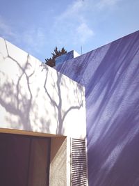 Low angle view of trees shadow on white house wall against sky