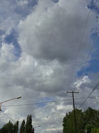 Low angle view of electricity pylon against cloudy sky