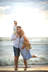 Full length of family standing on shore at beach against sky