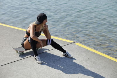 Woman sitting on skateboard at road by sea