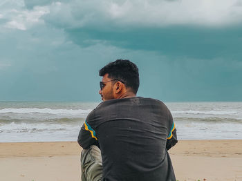 Rear view of man standing at beach against sky