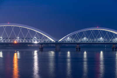 Illuminated bridge over river against blue sky at night