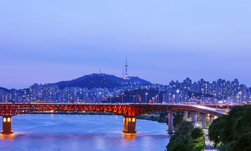 Illuminated bridge over river against sky at night