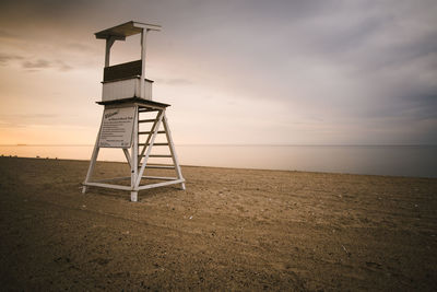 Lifeguard chair on beach against sky during sunset.
