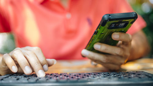 Midsection of man using mobile phone and computer on table