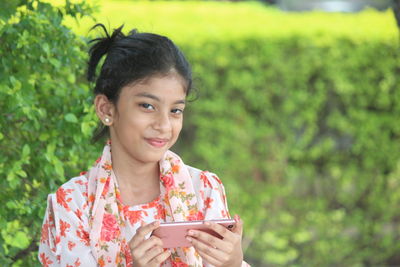 Portrait of smiling girl holding smart phone outdoors