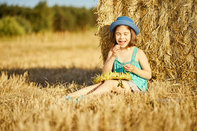 Happy girl sitting by hay on field