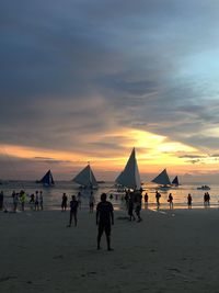 People at beach against sky during sunset