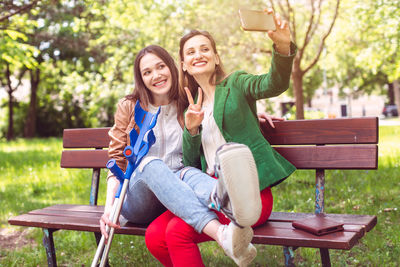 Portrait of smiling young woman using phone while sitting on bench