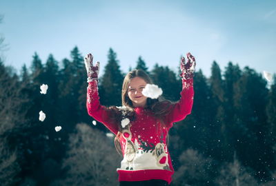 Smiling girl throwing snow while standing outdoors