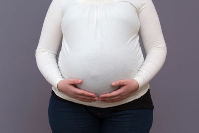 Midsection of woman touching face against gray background