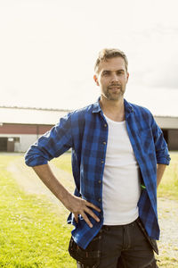 Portrait of handsome man standing with hand on hip at farm