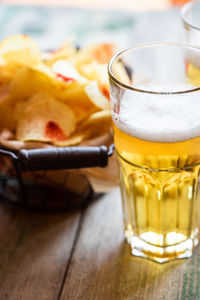 High angle view of fresh potato chips in metal basket by beers on table