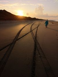 Man walking on beach against sky during sunset