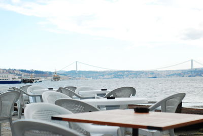 Chairs and table by sea against sky in city