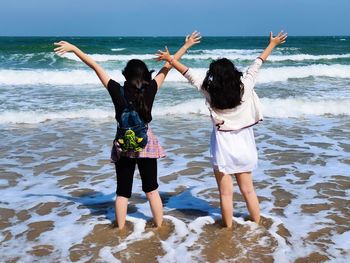 Rear view of two girls standing on the beach and raised arms 