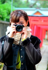 Portrait of woman holding camera standing outdoors