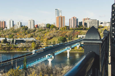 Bridge over river by buildings in city against sky