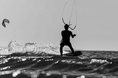 Full length of silhouette man kiteboarding in sea against sky