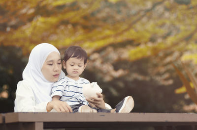 Mother and son holding piggy bank on table