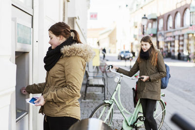 Young woman at cash machine with female friend in background