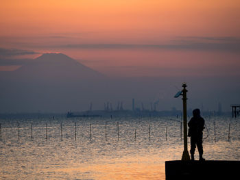 Silhouette man fishing while standing over sea during sunset