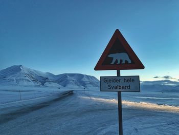 Road sign by snow covered mountain against clear blue sky