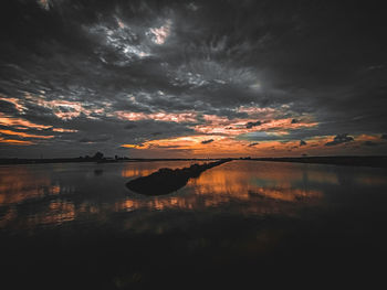 Scenic view of lake against dramatic sky during sunset