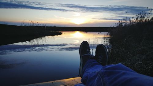 Low section of man relaxing on pier by lake at sunset