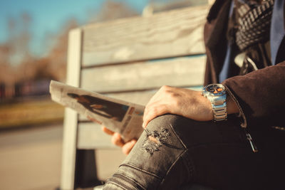 Midsection of man reading newspaper while sitting outdoors