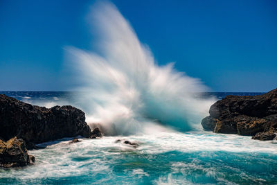 Sea waves splashing on rocks against sky