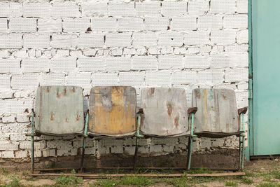 Old rusty movie theater chairs stand against a brick wall.