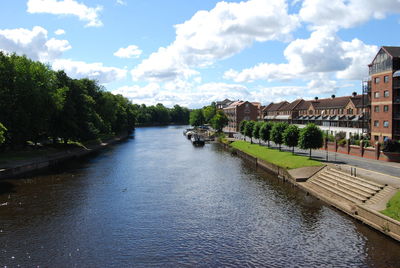 Canal amidst trees and buildings against sky