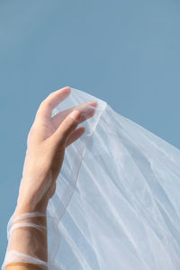 Low angle view of hand holding bottle against blue sky