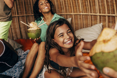 Happy girl taking coconut while sitting with family in wicker hut