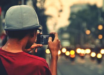 Rear view of man photographing camera in city