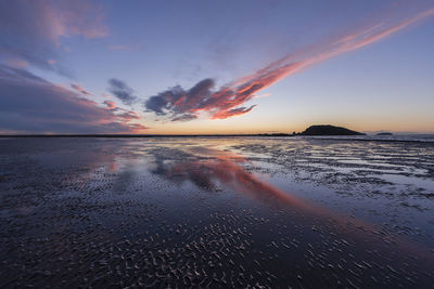 Scenic view of beach against sky at sunset