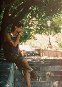 Side view of young man sitting by tree