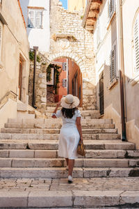 Rear view of young woman in white summer dress walking in street of picturesque old town