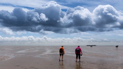 Rear view of men walking on beach against sky