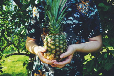 Midsection of woman holding fruit against plants