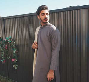 Fashionable young man wearing traditional clothes standing against wall