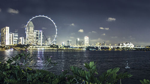 Illuminated ferris wheel in city against sky