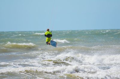 Rear view of man kiteboarding in sea against sky on sunny day