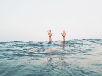 Cropped hands of person emerging from sea against clear sky