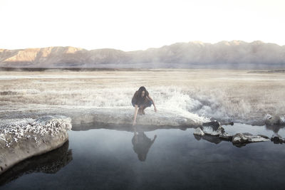 Woman touching water at mammoth lake hot springs against mountains