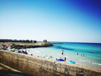 People on beach against clear blue sky